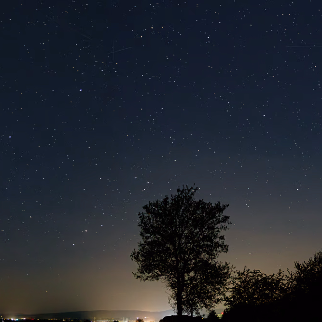 Nachthimmel am Benther Berg, 26.4. 4:00 Uhr, Am Hapkenberge, Baum im Vordergrund, die Lichter von Gehrden im Hintergrund. Am Himmel der Stern Antares, ein Hauch Milchstrasse