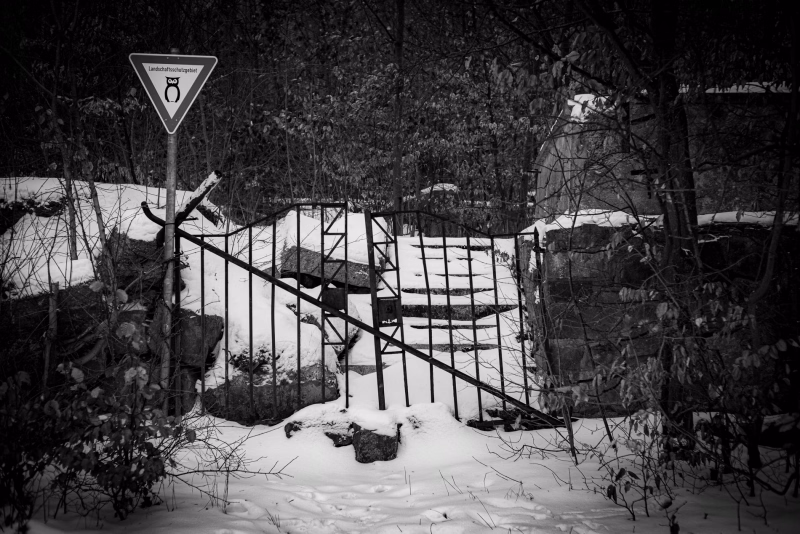 Das alte Eingangsportal vom Benther Berg Gasthaus. Verfallene Mauern und Treppen. Schnee auf den Stufen. Das alte Eisentor verrammelt mit einem Eisenrohr. Davor ein Schild Landschaftsschutzgebiet.